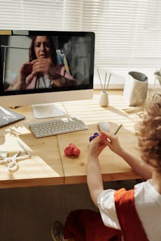 A child engaging in an online arts and crafts class, learning from home with clay and a computer.