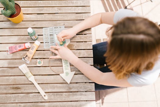 A person engaged in an outdoor crafting and painting activity on a wooden table.