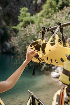 Close-up of a hand picking a safety helmet by a serene waterbody, showing outdoor adventure readiness.