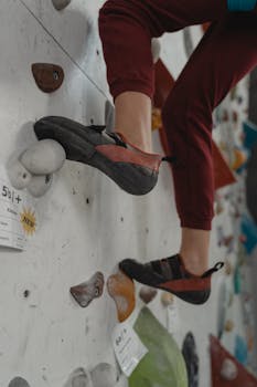 Close-up of legs in climbing shoes on an indoor wall with colorful grips.