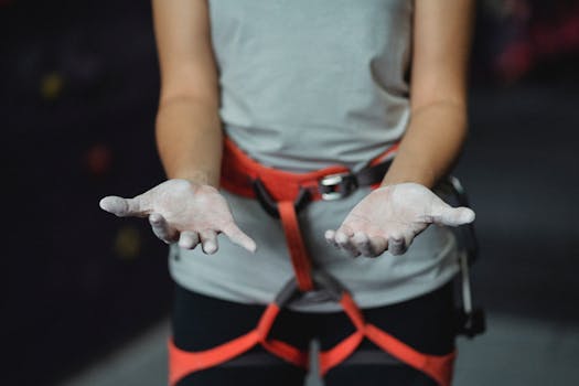 Crop anonymous slender female alpinist with safety harness demonstrating hands in talcum powder before practice