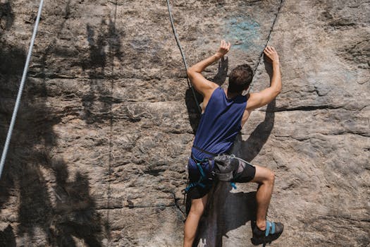 Determined man climbing a rock wall with safety harness and ropes, showcasing adventure and strength.