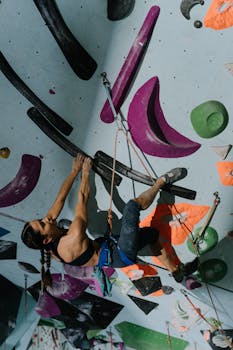 Empowered woman climbing an indoor gym wall, showcasing strength and athleticism.