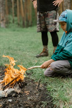 Young boy learning to manage a campfire with adult supervision in Russian outdoors.