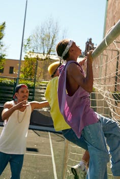 Young men enjoying outdoor sports activity, climbing a fence on a sunny day.